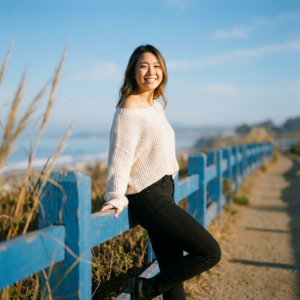 電影感、外景特寫人物肖像,16:9比例,4K超高解析度:
場景設定於溫暖柔和的秋日下午,陽光灑落在海邊蜿蜒小徑上,光線溫柔金黃。一位年輕亞洲女性作為主角,擁有甜美明亮的微笑,肌膚細膩、面容生動自然,眼中蘊含溫暖的神采。她穿著一件質感細膩、寬鬆舒適且露肩的米白色短版毛衣,下身搭配貼身黑色牛仔褲,整體造型時尚休閒、比肩電影主角。
她輕鬆自然地斜倚在一道鮮豔、復古感十足的藍色木製欄杆之上,姿態優雅隨性。畫面使用85mm焦段F1.4大光圈鏡頭,中景3/4身構圖,主體人物清晰細緻、膚質呈現柔和光澤感。前景有一層淡淡、模糊的蘆葦或芒草,透過淺景深帶來層次感與夢幻氛圍。背景遠處則是晃動的模糊海岸線與蔚藍晴空,景色朦朧詩意。
整體色調以溫暖自然、略帶金色餘暉為主,黑柔濾鏡效果減低對比,尤其在高光處展現細膩的光暈與膚質柔化,氛圍極具電影感和藝術氛圍。畫面細節豐富,請強調人物情感表達與場景的詩意氛圍。